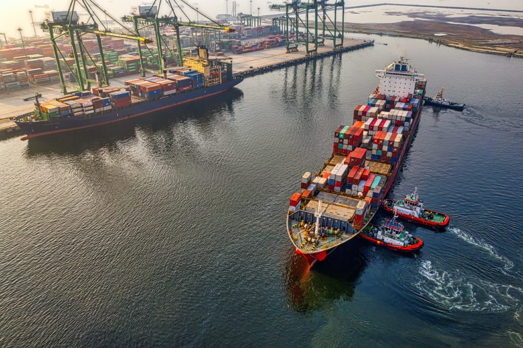 Photo of container ship being moved by tugboats
