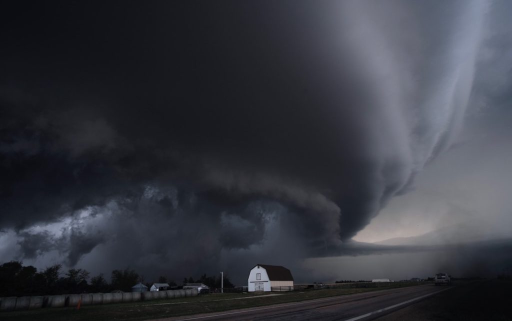 Photo of a massive swirling thunderstorm over a tiny barn
