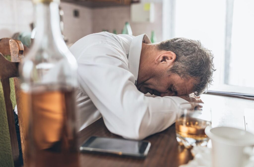 Photo of man passed out with a bottle of liquor on table