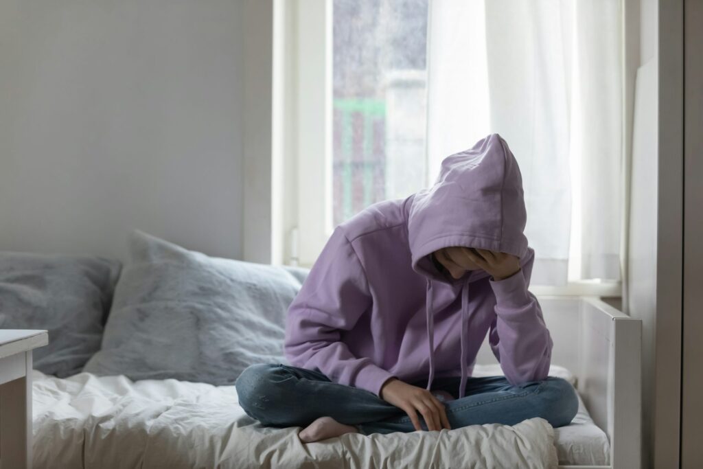 Photo of a teenager sitting on a bed.