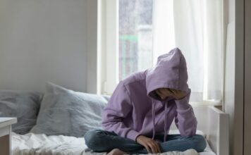 Photo of a teenager sitting on a bed.