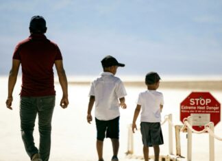 Photograph of a man and his son's entering the desert, next to a sign warning of dangerous heat