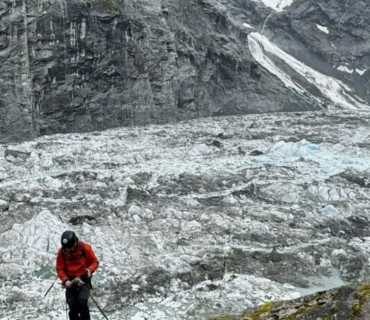 Photo of researcher descending into empty glacial valley.